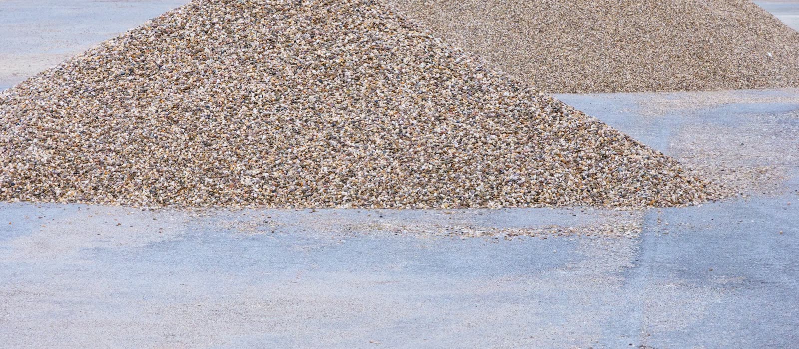 Piles of decorative gravel on the concrete hardstand of a landscape supply yard.