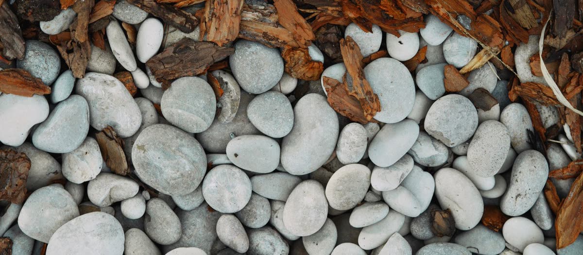 Smooth grey pebble and reddish bark mulch meeting, seen from above.